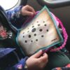Niña sosteniendo el tablero del Nonaga de Carabachuis en un transporte, juego portátil de estrategia