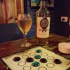 Tablero del Dao de Carabachuis desplegado en mesa de bar, junto a una copa y botella de bebida