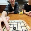 Jugador moviendo una ficha verde en el tablero del Neutrón de Carabachuis, juego abstracto portátil con fichas blancas y negras.
