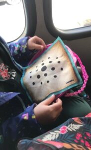 Niña sosteniendo el tablero del Nonaga de Carabachuis en un transporte, juego portátil de estrategia