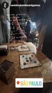 Juego abstracto Dao desplegado en un evento de juegos de mesa en Brasil, con jugadores observando la partida