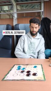 Alexis yendo en tren hacia Berlín, Alemania, frente al tablero portátil del Dao de Carabachuis con piezas de vidrio
