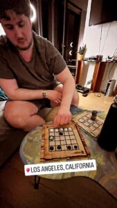 Jugador moviendo fichas en el tablero del Neutrón de Carabachuis en Los Ángeles, juego abstracto portátil.