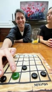 Jugador moviendo una ficha verde en el tablero del Neutrón de Carabachuis, juego abstracto portátil con fichas blancas y negras.