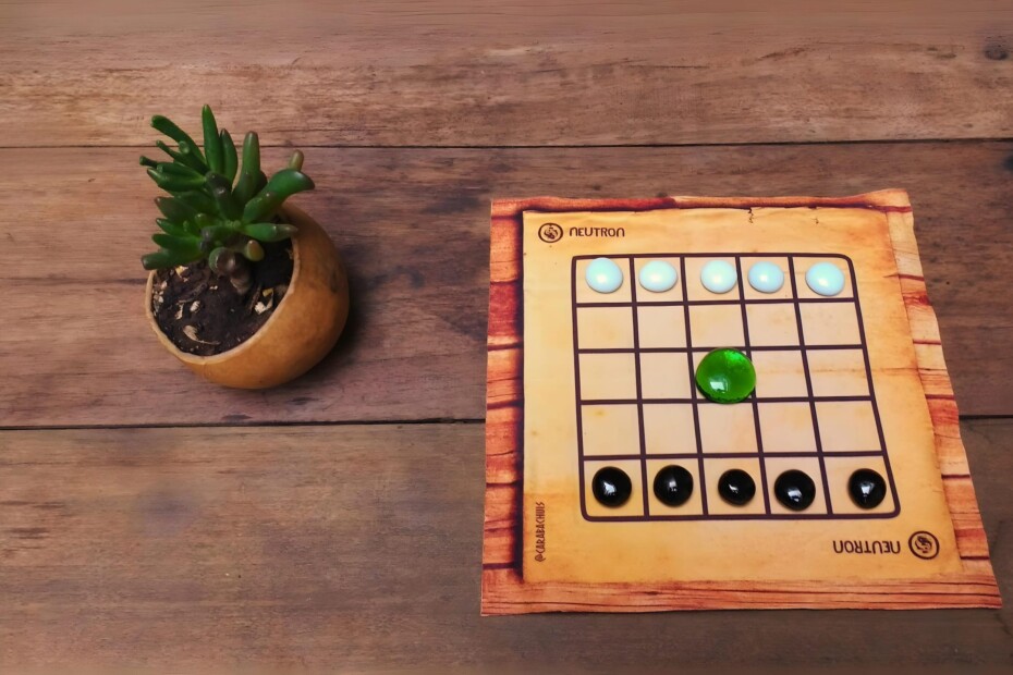 Tablero de Neutron dispuesto sobre mesa de madera junto a pequeña maceta con suculenta, transmitiendo la esencia de 'Juegos que Viajan' con un toque natural y acogedor