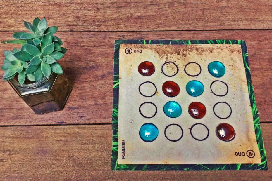 Portada del Dao, el juego extendido en su posición inicial, con una plantita decorativa al lado.